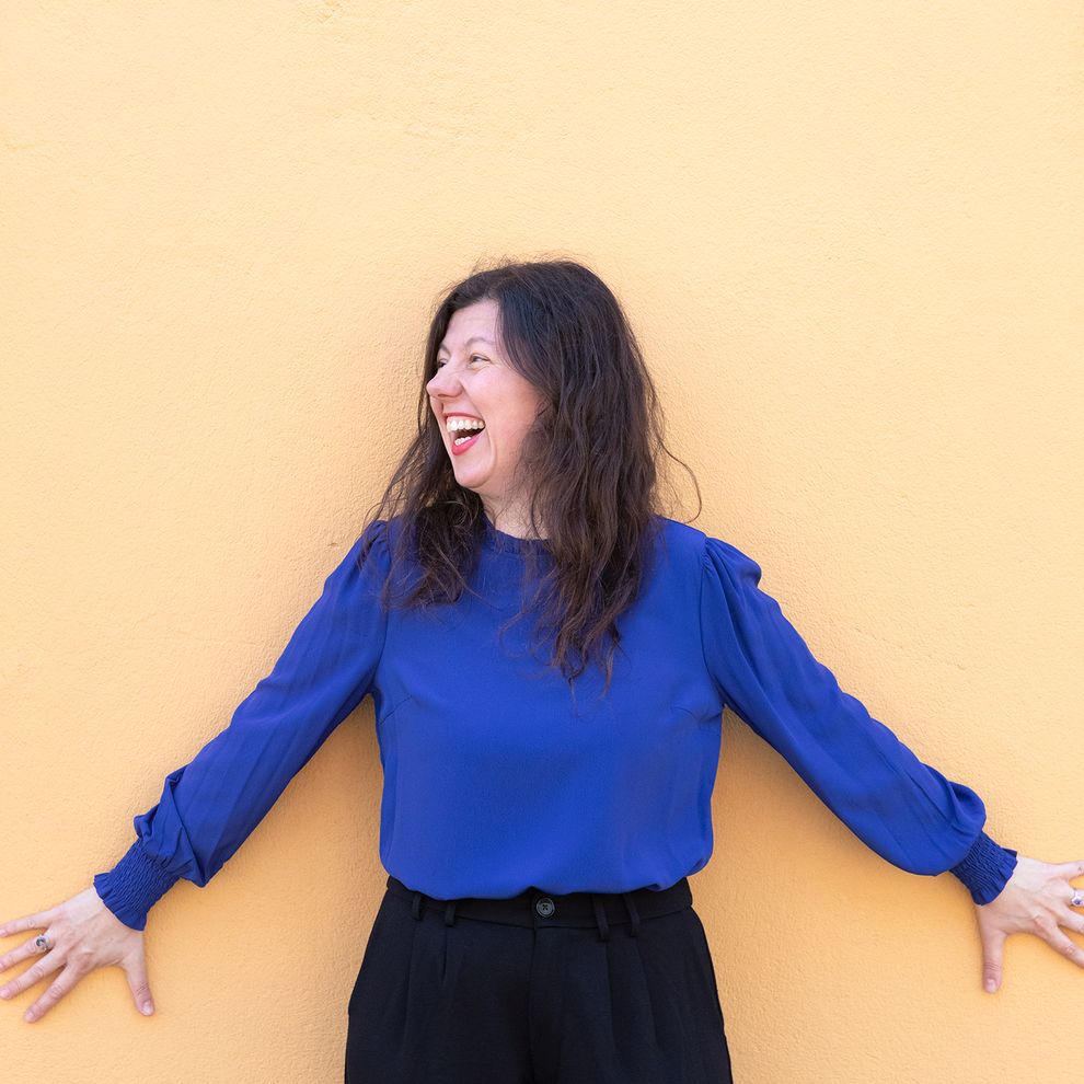 Alma Kirlic står med händerna mot en gul husvägg och skrattar